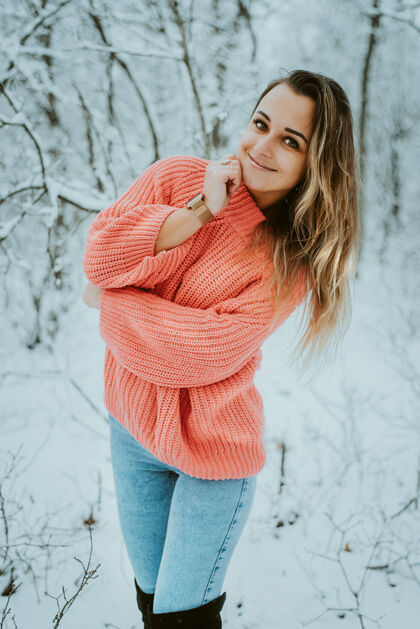 牛仔裤一个穿着粉色宽松毛衣和牛仔裤的漂亮女孩在寒冷的雪域森林里女孩快乐心情