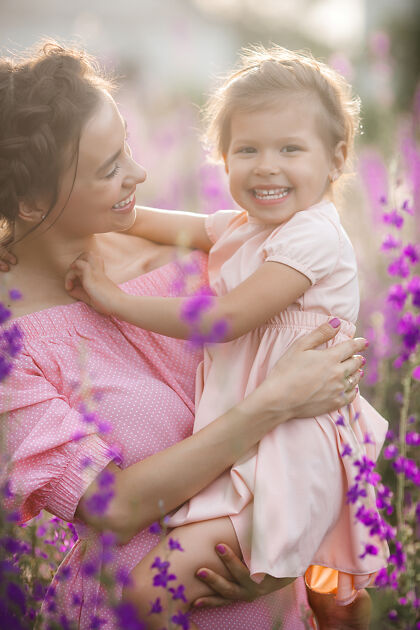 无忧无虑年轻漂亮的妈妈和她的小女儿一起在户外玩耍花紫罗兰色花坛特写成人可爱