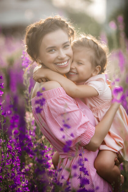 女儿年轻漂亮的妈妈和她的小女儿一起在户外玩耍花紫罗兰色花坛女孩家庭孩子