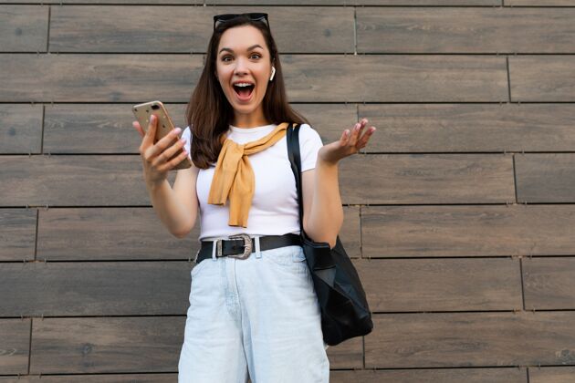 兴奋照片中的年轻女子穿着休闲服 站在街上用手机看着镜头使用高兴电话