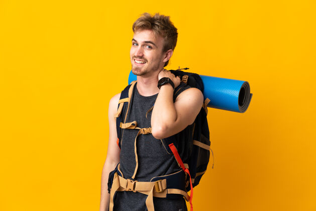 男人年轻的登山者背着一个大背包 在黄色的背景上笑着徒步旅行年轻人旅行
