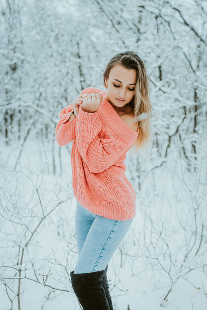 寒冷一个穿着粉色宽松毛衣和牛仔裤的漂亮女孩在寒冷的雪域森林里公园裤子模特