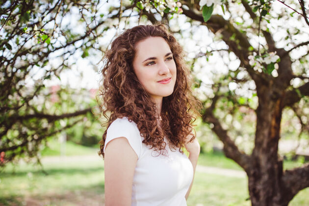 户外在盛开的苹果树下 快乐的卷发年轻女子穿着白色t恤街道可爱开花