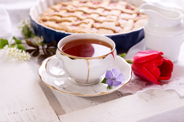 奶酪一杯白瓷茶 新鲜出炉派.英国早餐静物与饮料和招待 红色郁金香花和白色桌布英国花奶油