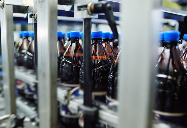 很多塑料pet瓶由黄色塑料制成 蓝色瓶盖 背景是传送带上的啤酒或甜饮料工厂.工业食品饮料生产大型输送带工业