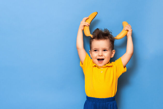欢呼快乐的肖像画 一个孩子带着迷人的微笑 穿着黄色t恤 手里拿着一根香蕉 在摄影棚拍摄可爱表情美味