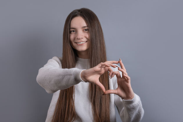 女士一位年轻迷人的微笑女子用双手展示心形的肖像休闲保健手指