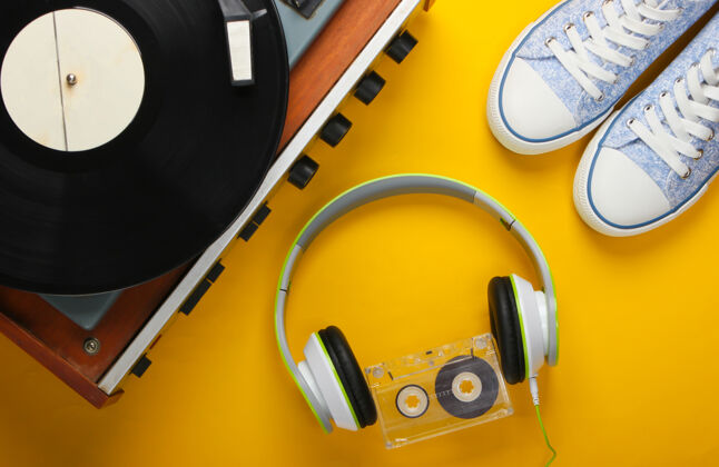 Dj旧的乙烯基录音机与立体声耳机 录音带和黄色表面的运动鞋电子转盘播放