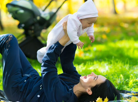 一起在公园里郁郁葱葱的草地上 一位笑着的母亲正和她的小女儿躺在毯子上玩耍快乐新生儿可爱