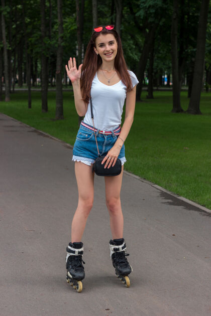 公园可爱快乐的女人站在辊臂上挥手微笑短裤黑发滚轴溜冰鞋
