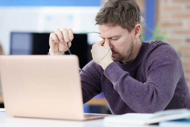 职业疲惫的男人坐在笔记本电脑屏幕前 手里拿着眼镜忙碌计算机经理