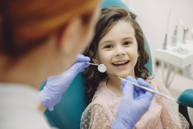 牙科一个可爱的小女孩笑着看着坐在口腔科座位上的相机 而儿童口腔医生正准备做牙齿检查的画像保健专业工作