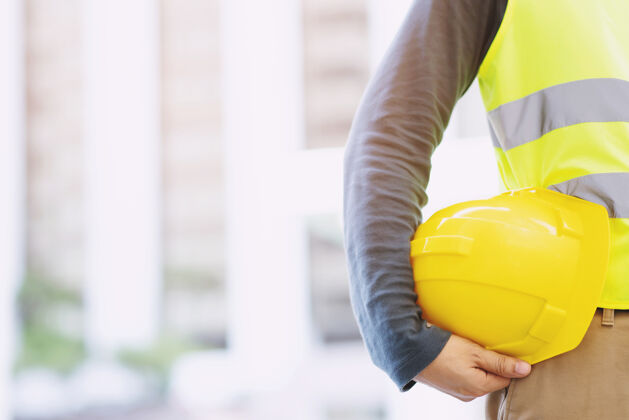 商业工程男施工人员手持黄色安全帽 穿着反光服 工作安全室外操作建造桌子的方法建筑设备承包商