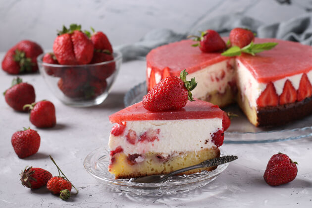 鞭子自制芝士蛋糕和草莓和果冻在灰色的表面和切片蛋糕在盘子里的前景水果灰色背景甜