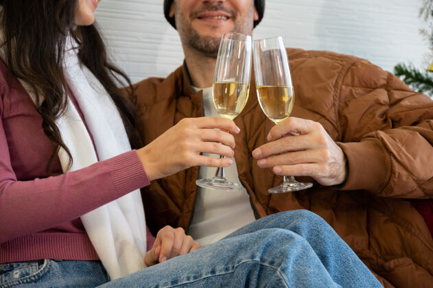 欢呼浪漫微笑的情侣坐在沙发上 在客厅里碰杯香槟房间圣诞节新年和爱情的概念饮料杯子房子