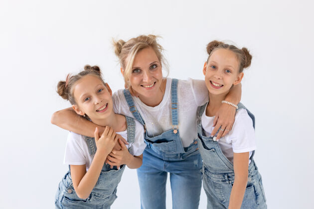 妈妈人 家庭和孩子的概念-一个可爱的母亲在白色表面拥抱她的双胞胎女儿的肖像女人父母魅力