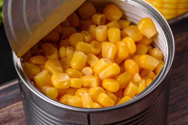 甜玉米新鲜美味的散装玉米罐头放在深色混凝土背景的木质砧板上金色容器营养
