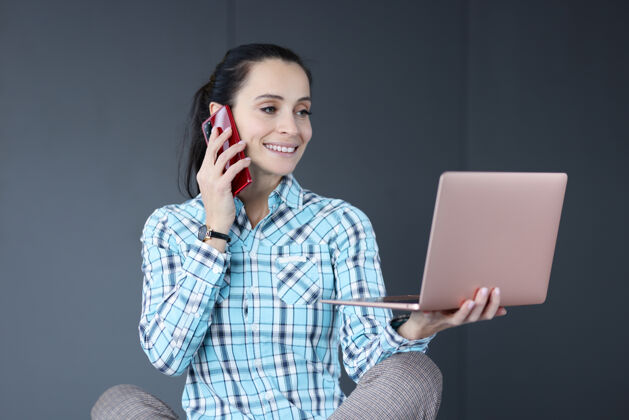 设备年轻女子手里拿着笔记本电脑 说着话电话自由职业者工作理念快乐技术手机