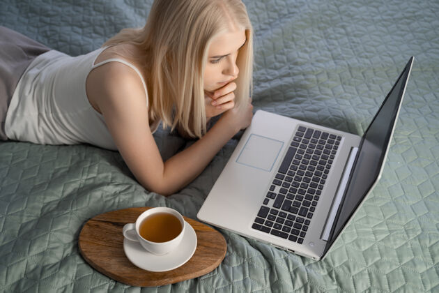 坐着在床上使用笔记本电脑的女人互联网笔记本室内