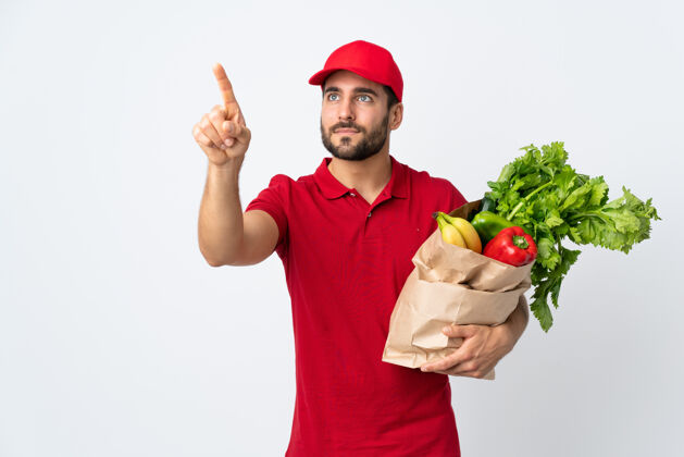 男人一个留着胡子的年轻人拿着一个装满蔬菜的袋子 隔离在白色的背景上 触摸着透明的屏幕送货素食成人