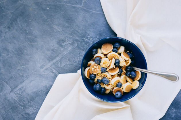 小吃迷你煎饼麦片特写镜头 深蓝色碗里的迷你煎饼 枫叶糖浆蜂蜜和蓝莓早餐美食蓝莓