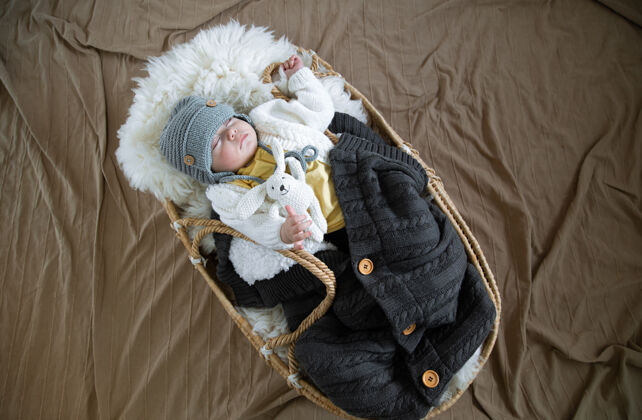 毛毯婴儿在柳条摇篮里睡得很香 在温暖的毛毯下戴着一顶温暖的针织帽子 把手上放着一个玩具新生儿幼儿孩子