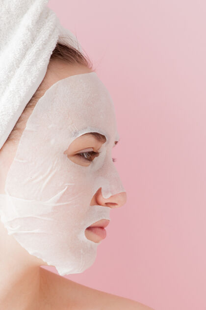 面部美丽的年轻女子正在一张粉红色的脸上敷化妆纸面膜皮肤科卫生光滑