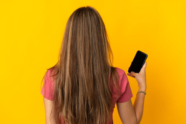 姿势年轻女子用手机把黄色背景隔离在后面的位置手机背部说话