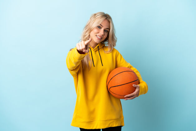 手指年轻的俄罗斯女子打篮球孤立在蓝指前与快乐的表情震惊运动员指着