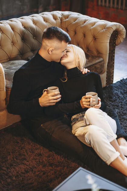 年轻迷人的年轻夫妇在地板上拥抱 倚在沙发上 微笑着亲吻圣诞节微笑杯子