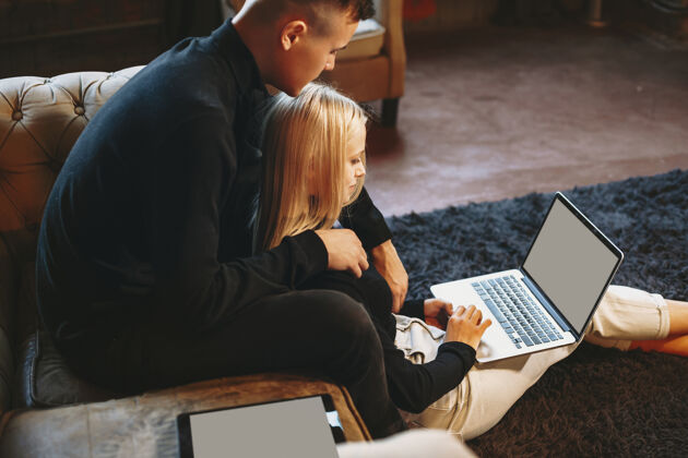 金发漂亮的年轻女性在家里拿着笔记本电脑在地板上工作 而她的男朋友正从背后拥抱着她情侣年轻家庭