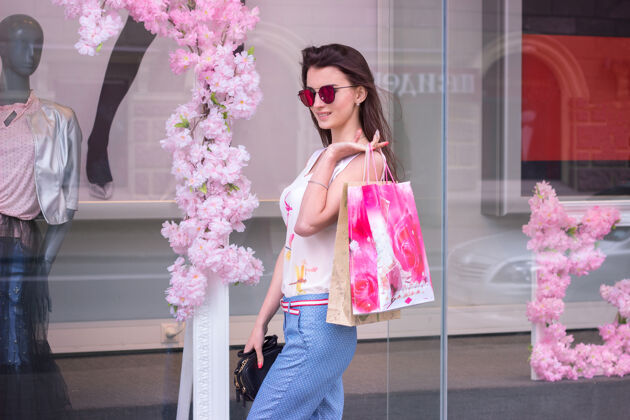 消费者可爱的戴眼镜的时髦女人站在城市的精品店附近 保管着包裹购买魅力控股