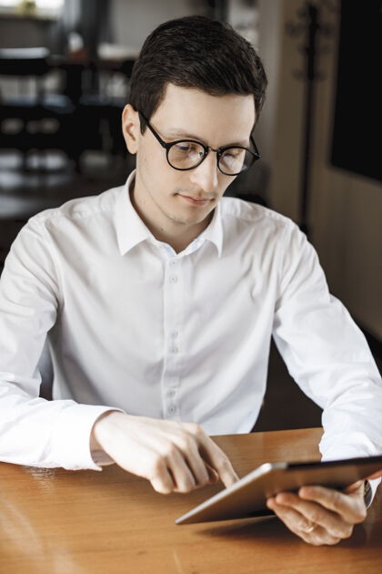 经理一个穿着白衬衫戴着眼镜坐在梳妆台旁使用平板电脑的英俊年轻人的画像房子通信工人