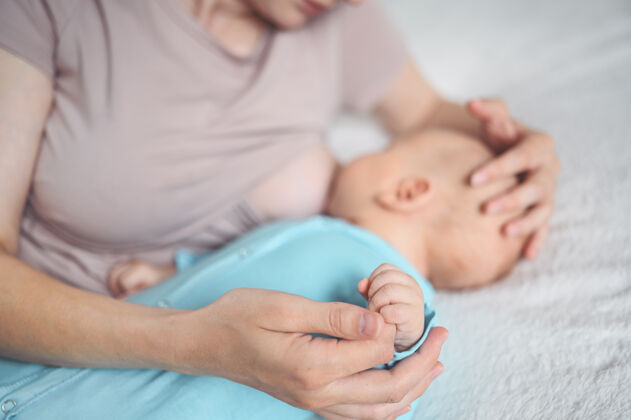 喂养年轻的母亲躺在床上 抱着一个穿着蓝色连体衣的可爱的新生婴儿 用母乳给他喂奶婴儿营养吃