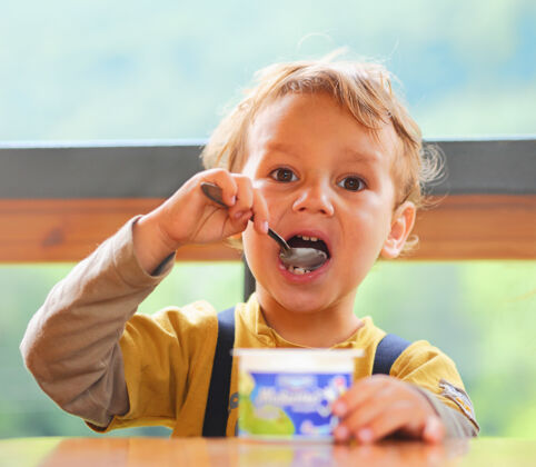 童年小男孩正在吃酸奶 手里拿着勺子 坐在桌边餐孩子早餐