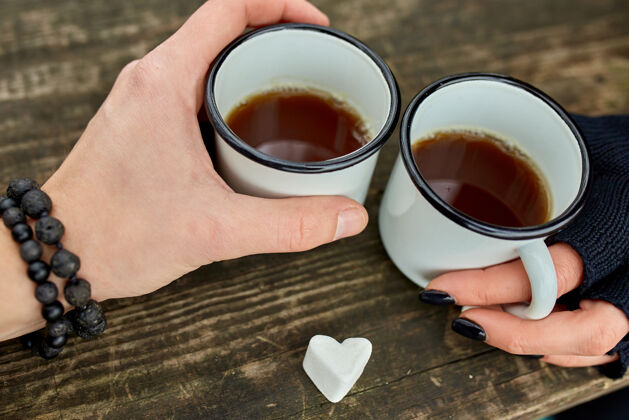 女人两杯茶在大自然中的情侣手中 戴着黑手套放在木头表面男人饮料感觉