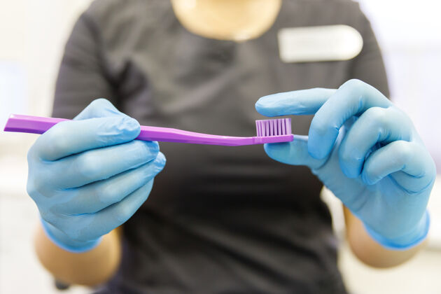 手女牙医或口腔医生拿着紫色牙刷并展示 显示刚毛僵硬展示塑料口腔