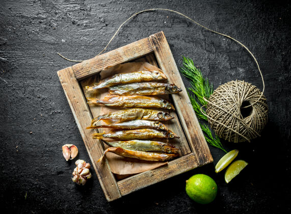 麻绳烟熏鱼放在盘子里 用石灰 旧麻绳和大蒜开黑色乡村背景食物自然酸橙