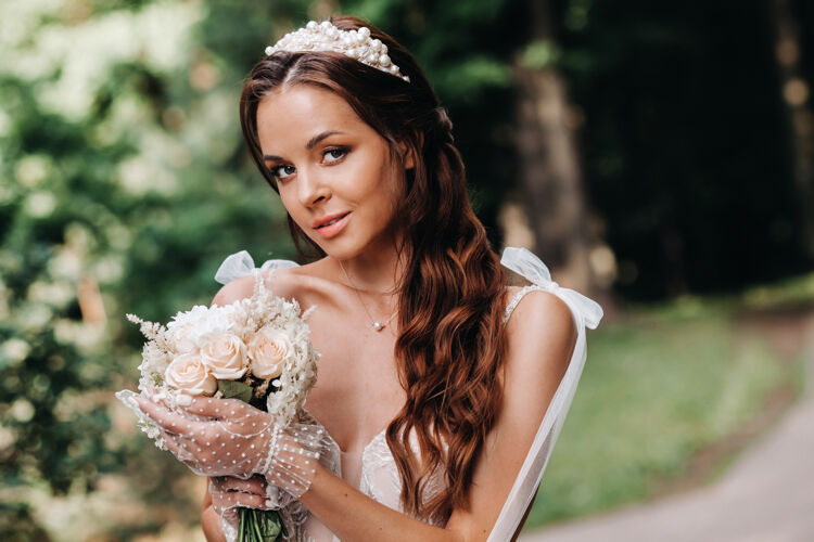 手套一个优雅的新娘在一个自然公园里穿着白色的裙子和一束花束的肖像公园水模型