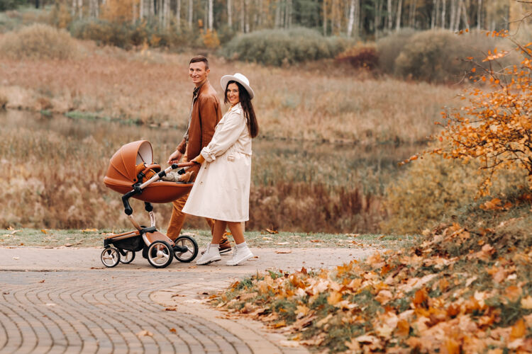 帽子秋日里 爸爸妈妈和婴儿车在散步停车场金秋时节 一家人走过自然公园母亲丈夫婴儿睡眠