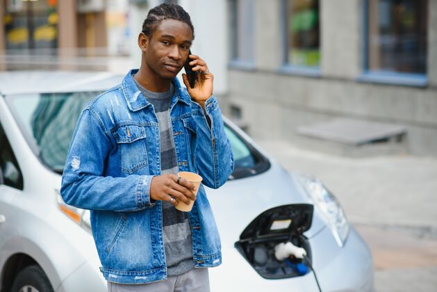 年轻人男人在等待时使用智能手机 电源连接到电动车上为车内的电池充电社交媒体加油服务