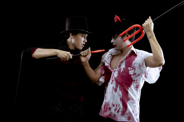 玩具年轻的亚洲男子在服装地狱 邪恶和巫师与斗争的黑色墙壁与万圣节时尚节的概念两个青少年亚洲男子在角色扮演万圣节血化妆青少年