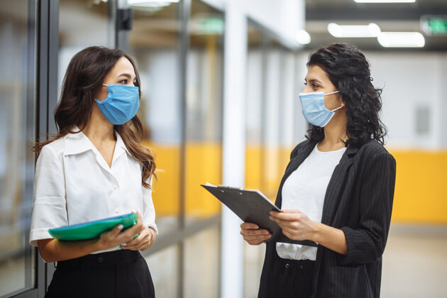 平板电脑两位女商人穿着医用无菌衣在办公室讨论工作问题面具新的正常 健康和安全措施理念冠状病毒工人笔记本电脑