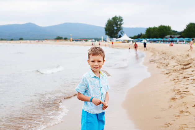 海洋海滩上穿着衬衫和短裤的小男孩沙子很少男孩在热带海滩上玩得很开心度假热带假日