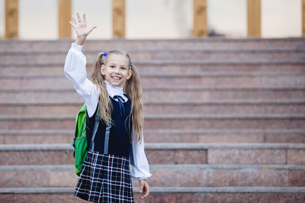 女学生十几岁的女学生穿着制服 扎着辫子 背着一个格子裙的背包 在学校入口处的楼梯上挥手青少年孩子教育