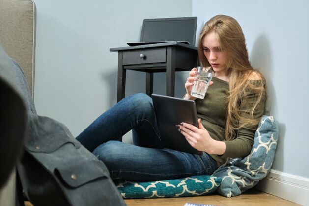 在线年轻女子坐在家里的地板上 拿着数码平板电脑 喝着一杯咖啡水女孩利用互联网学习 阅读 休息房子漂亮阅读