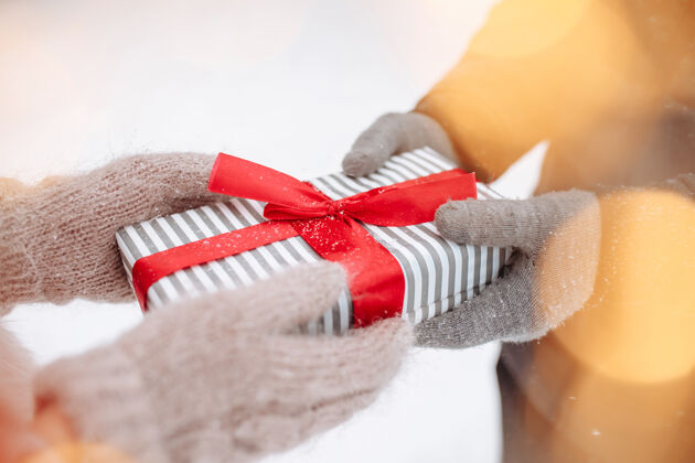 羊毛在下雪的冬天 一对恩爱的夫妇戴着羊毛手套在外面互相送礼物公园条纹一个男人手里拿着红色蝴蝶结的盒子瓦伦丁女士情人节概念女人情人节开放女性女朋友