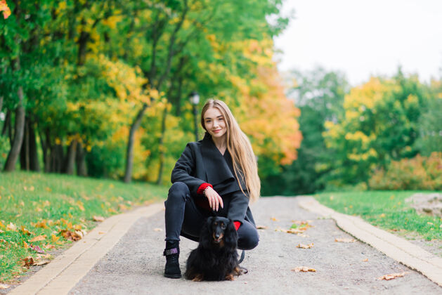 皮带秋天公园里日出时分 一位年轻迷人的女士抱着她的腊肠狗在户外女人团结纯种