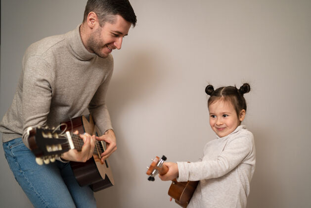 室内爸爸用手弹吉他女儿孩子学会用钢琴演奏乐器音乐导师父亲和孩子的二重唱亚洲人父母男人