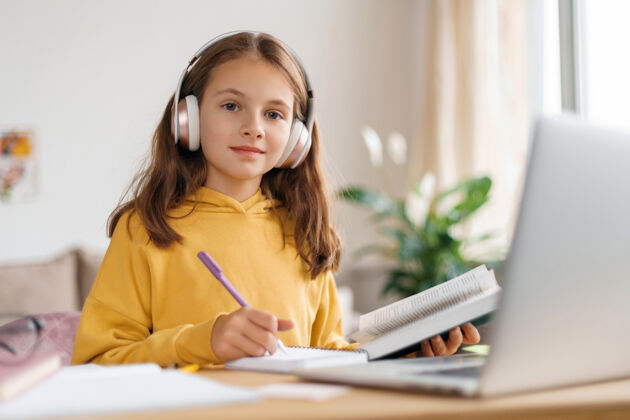 视频通话快乐的女孩戴着耳机 看着相机 用笔记本电脑和互联网做家务冠状病毒锻炼年轻